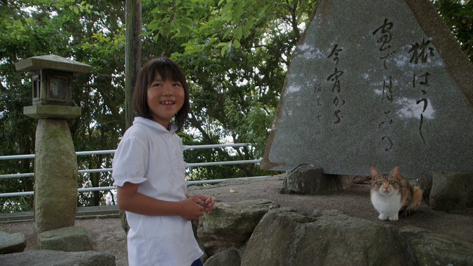 Ein Kind in weißem Hemd an einem Schrein sowie eine Katze
