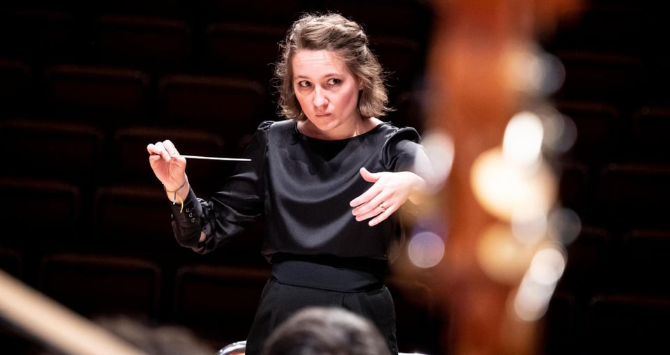 Eine Frau in schwarzem Kleid dirigiert ein Orchester