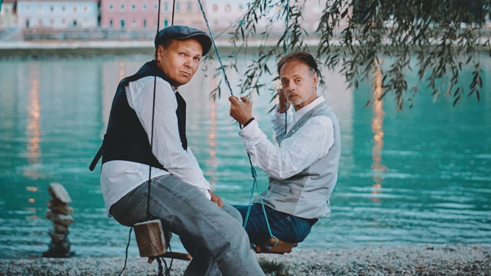 Foto für das Event BlöZinger - Das Ziel ist im Weg mit den beiden Künstlern auf einer Schaukel und einem Fluss im Hintergrund