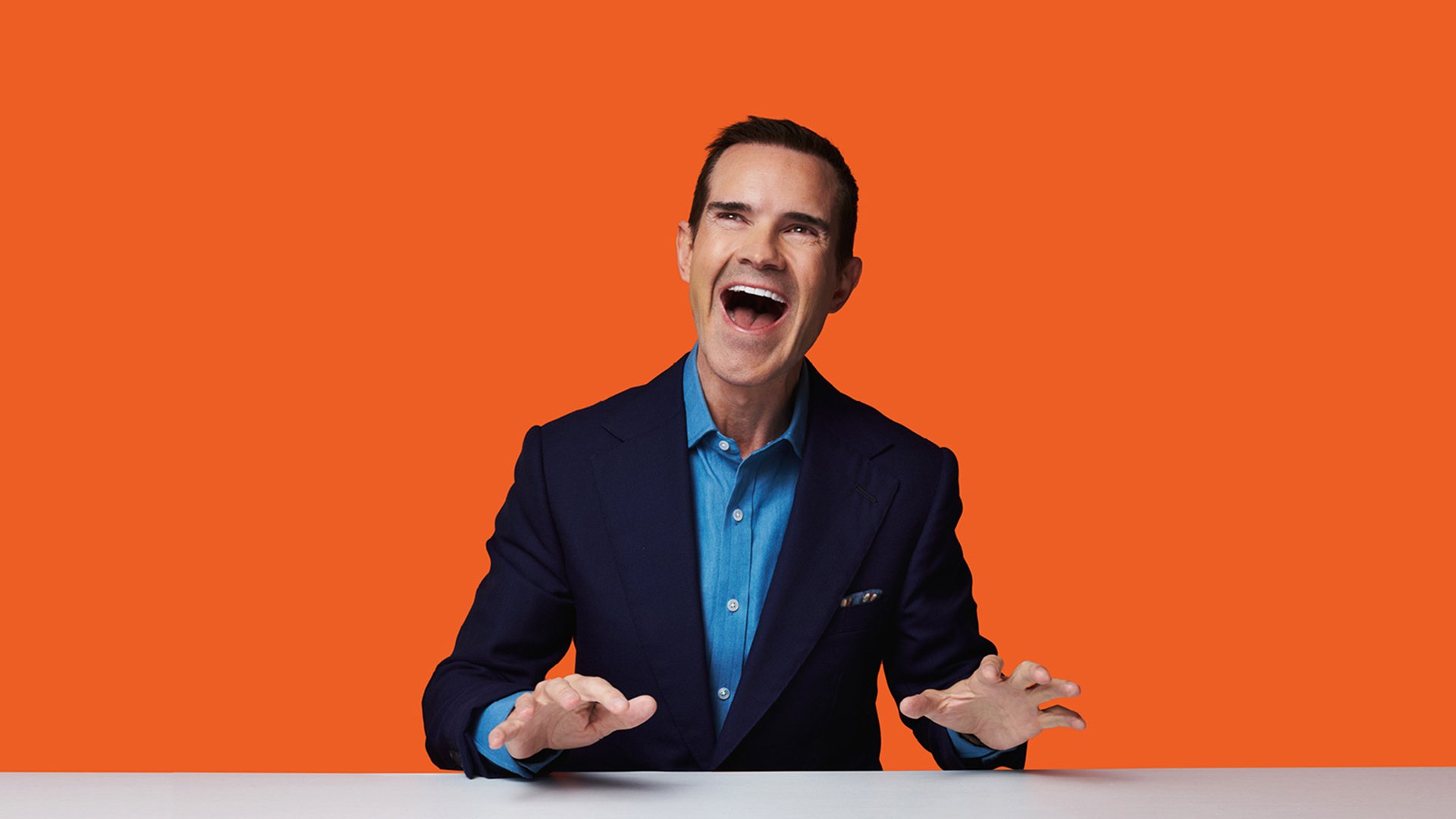 Foto für die Veranstaltung Jimmy Carr mit dem Künstler vor orangem Hintergrund.