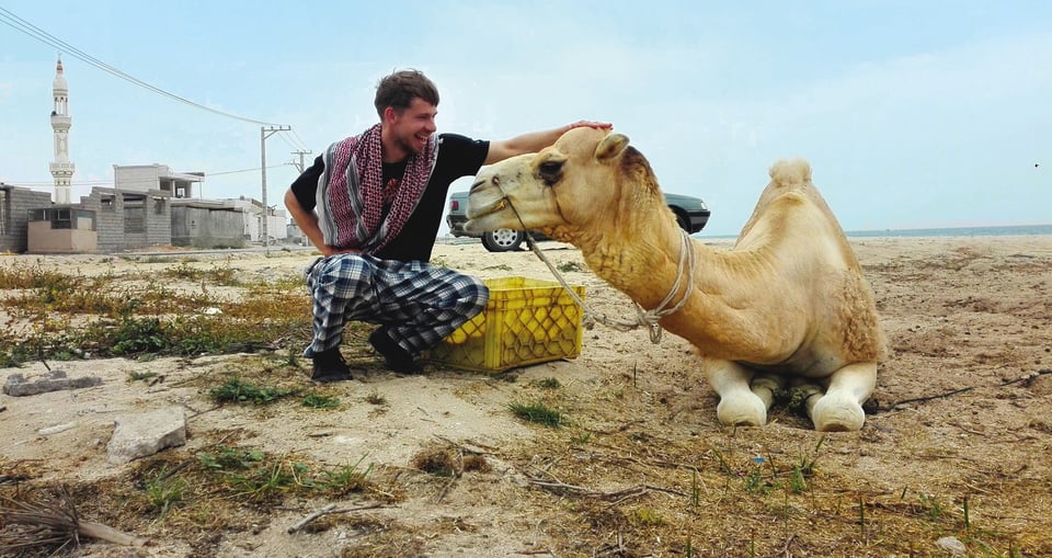Foto von einem Mann mit einem Kamel in einer Wüstenlandschaft.