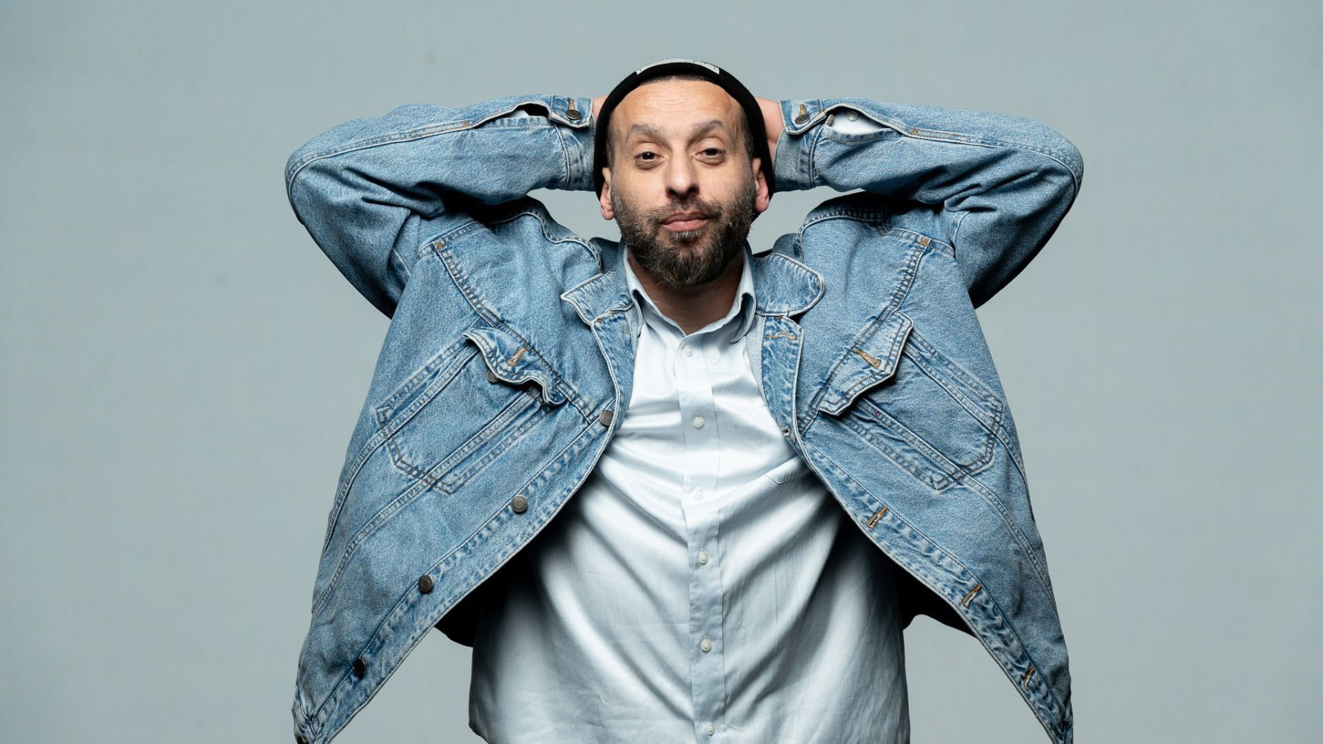 Foto für die Veranstaltung ‚Tamer Nafar‘ mit dem Künstler, der die Arme über dem Kopf hält, vor einem blauen Hintergrund.