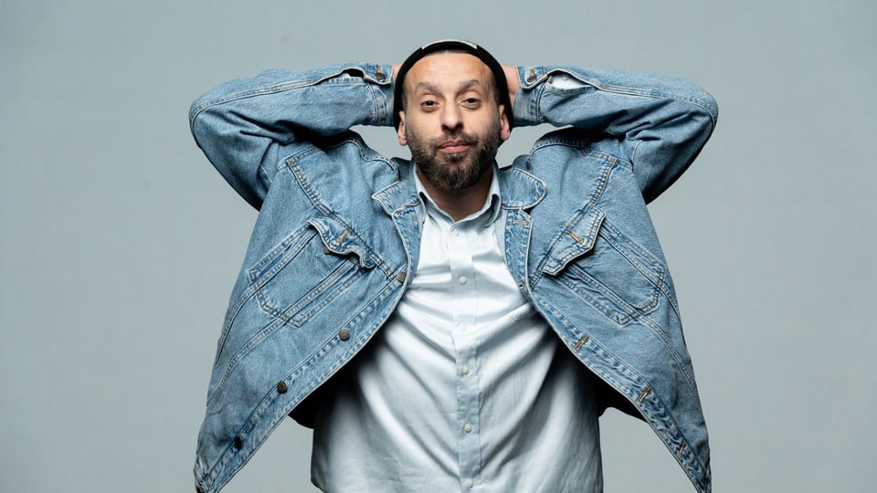 Foto für die Veranstaltung ‚Tamer Nafar‘ mit dem Künstler, der die Arme über dem Kopf hält, vor einem blauen Hintergrund.