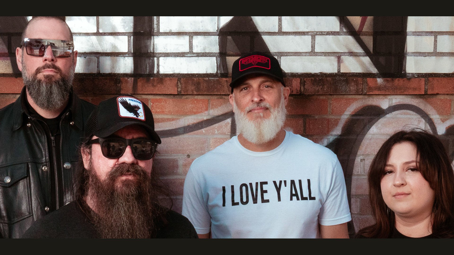 Vier Mitglieder der Band High Desert Queen stehen vor einer gemauerten Wand mit Graffiti, blicken in die Kamera, legere Kleidung, teilweise mit Bärten und Caps