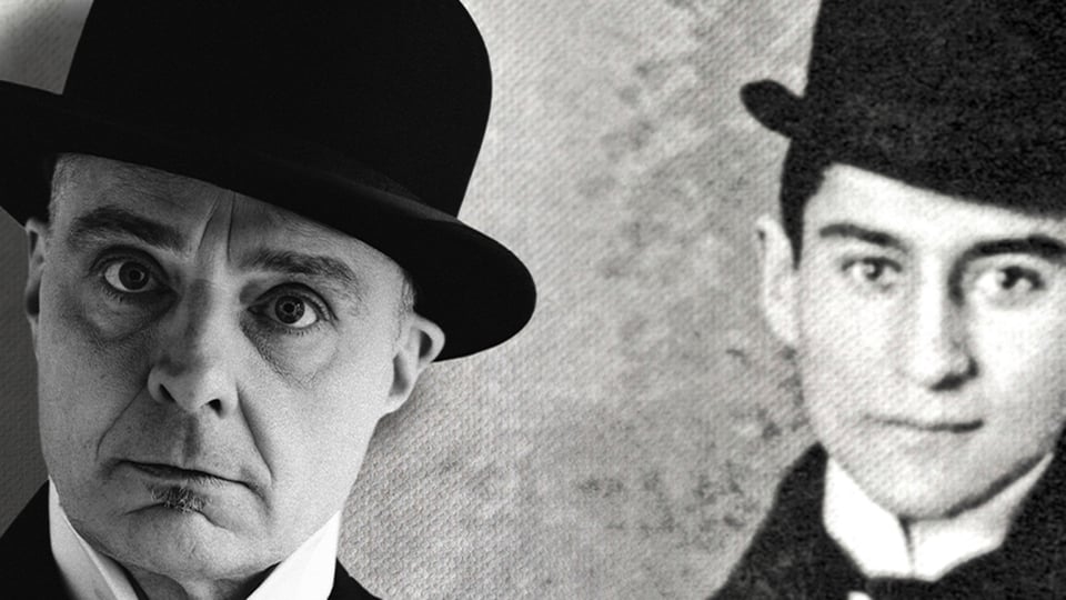 Zwei Personen mit dunklen Anzügen und Melone stehen nebeneinander vor einem grobkörnigen, schwarz‑weißen Hintergrund; die Kopfbedeckungen und Kragen sind klar erkennbar.