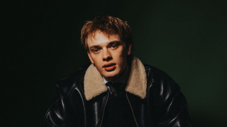 Der Künstler Levka in einer dunklen Lederjacke vor dunkelgrünem Hintergrund