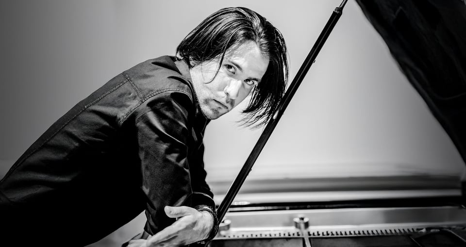 Schwarzweißfoto eines Jungen, der an ein Klavier gelehnt ist