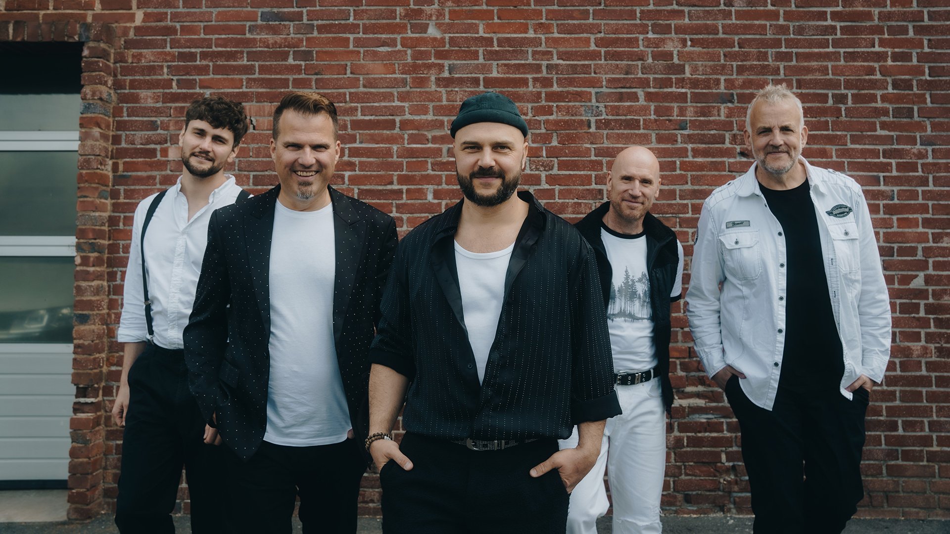 Fünf Musiker in schwarz-weisser Kleidung vor einer Ziegelwand