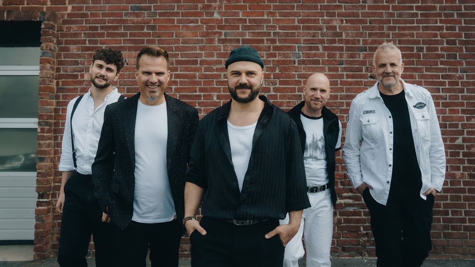 Fünf Musiker in schwarz-weisser Kleidung vor einer Ziegelwand