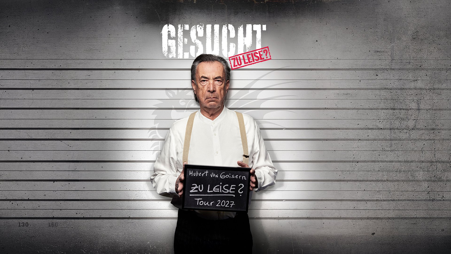 Eventmotiv zu Hubert von Goisern & Band – „Kapitel 1: Zu leise?“: Person steht frontal vor grauem Hintergrund mit Höhenlinien, hält eine Tafel mit der Aufschrift „Hubert von Goisern – Zu leise? Tour 2027“. Oben im Bild der Schriftzug „GESUCHT“ sowie ein roter Stempel „ZU LEISE?“.