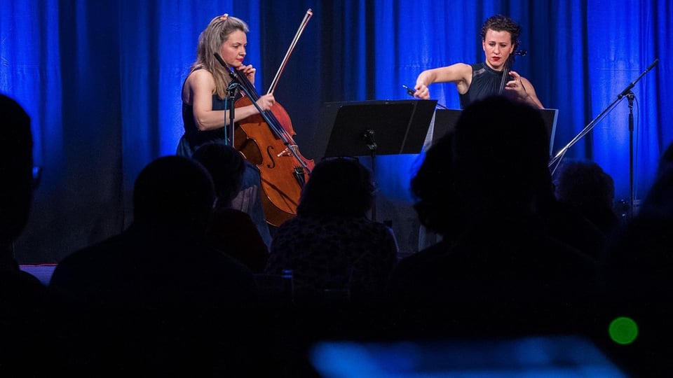 Cello-Duo spielt auf einer Bühne vor Publikum, klassische Musik mit blauer Beleuchtung und Konzertatmosphäre
