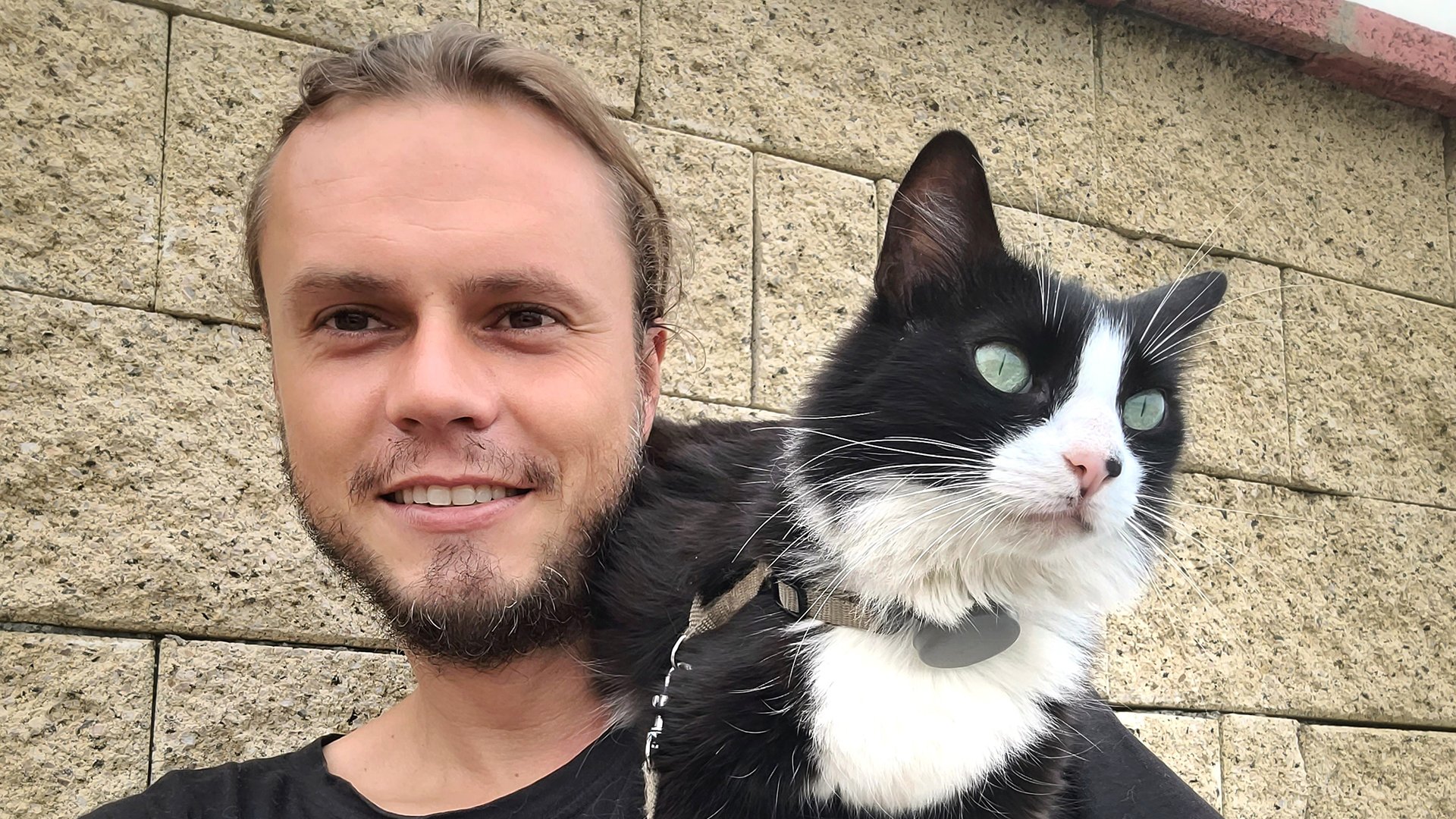 Martin Klauka mit einer schwarz-weißen Katze auf der Schulter vor einer Mauer