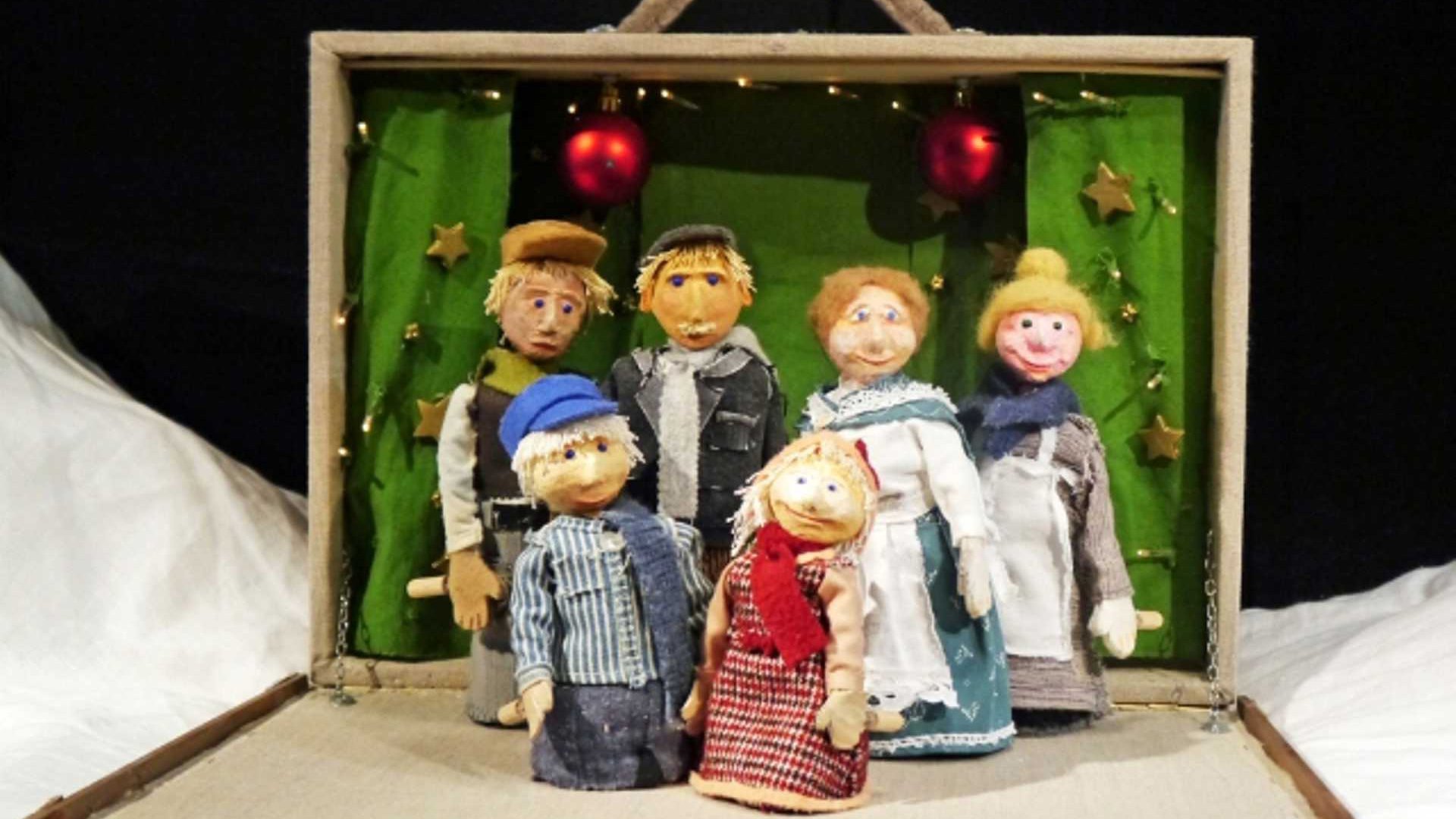 Bühnenbild aus Michel feiert Weihnachten mit sechs handgefertigten Figuren in Winterkleidung vor einer grünen Kulisse in einem geöffneten Puppentheaterkasten, dekoriert mit Sternen, Lichterkette und roten Christbaumkugeln.