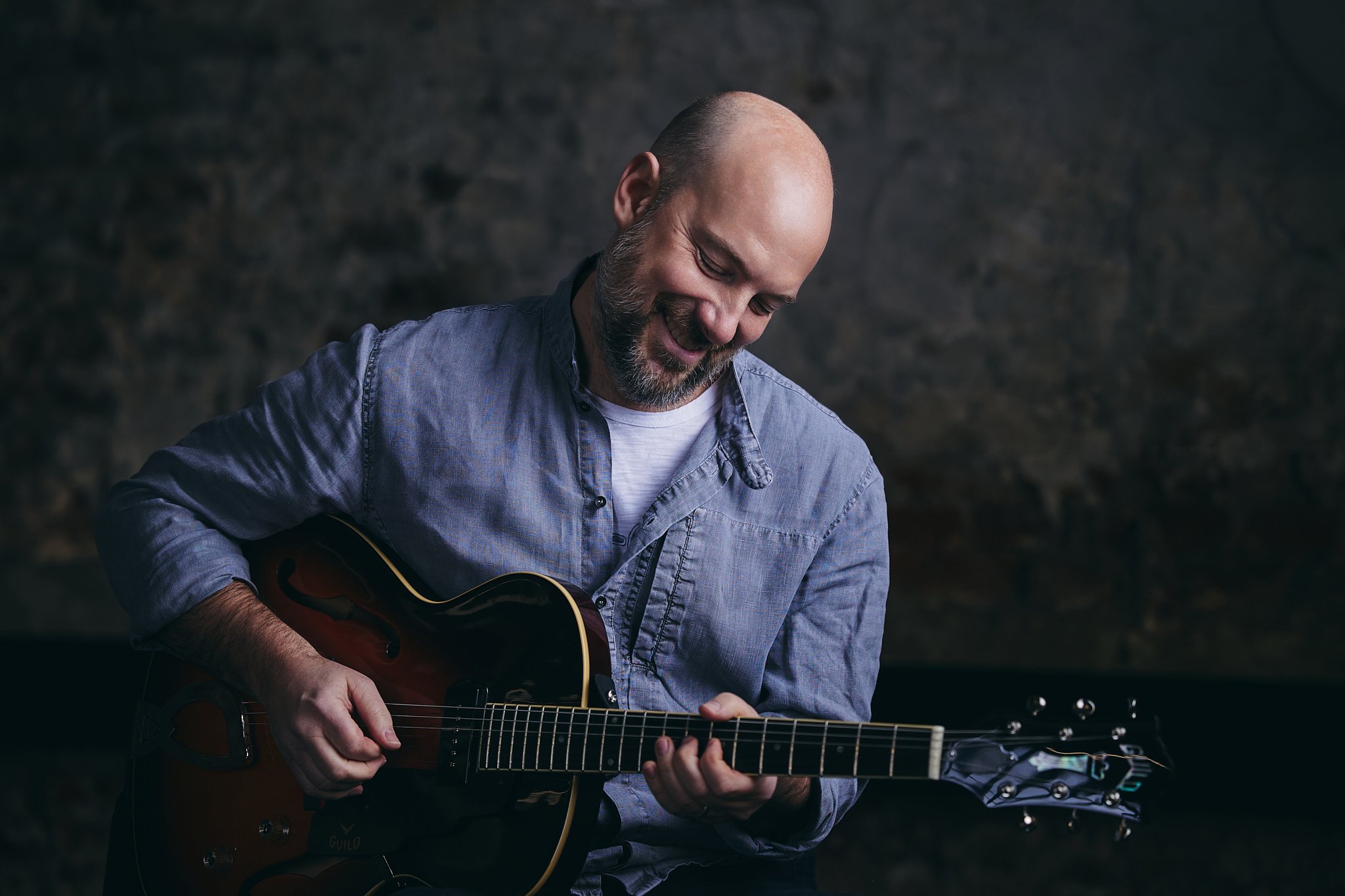 Stephan Zinner in Jeanshemd mit Gitarre vor dunkel marmoriertem Hintergrund
