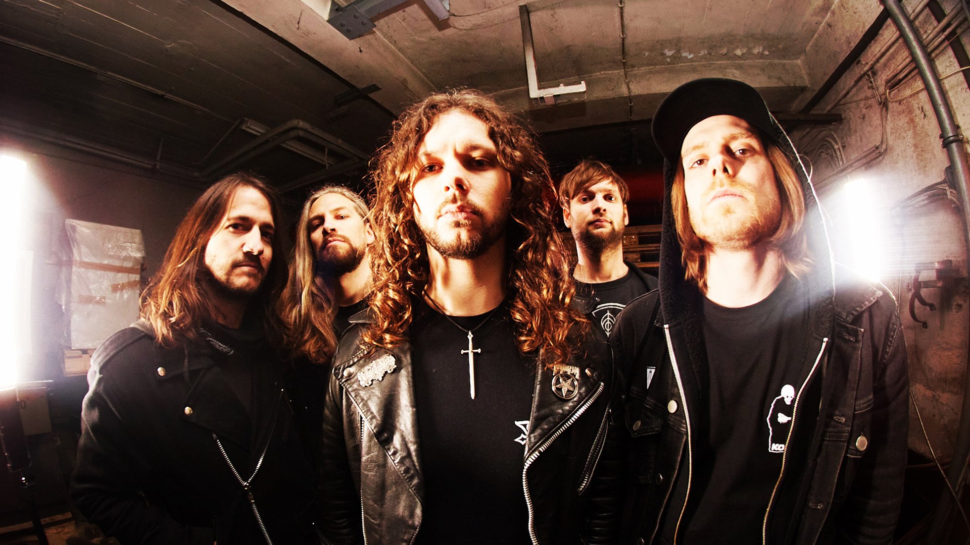 Bandporträt von fünf Musikern in dunklem Raum mit Lederjacken, lange Haare und starke Beleuchtung, Rock- und Metal-Ästhetik