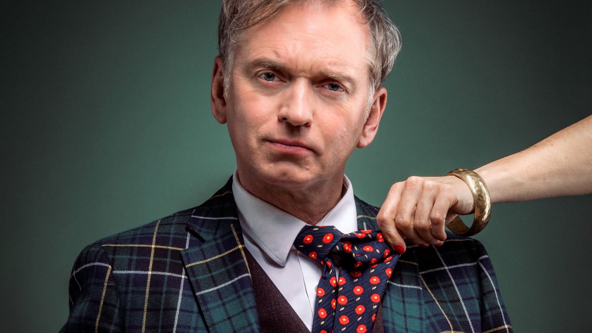 Der Künstler mit Kariertem Sakko und bunter Krawatte, an der ihn eine Hand zieht