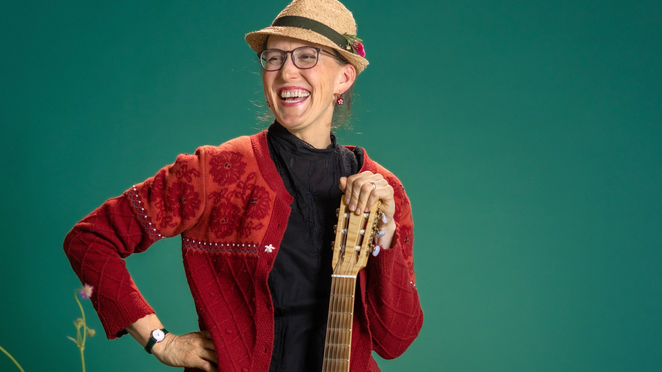 Die Künstlerin mit Strohhut und Gitarre vor türkisgrünem Hintergrund