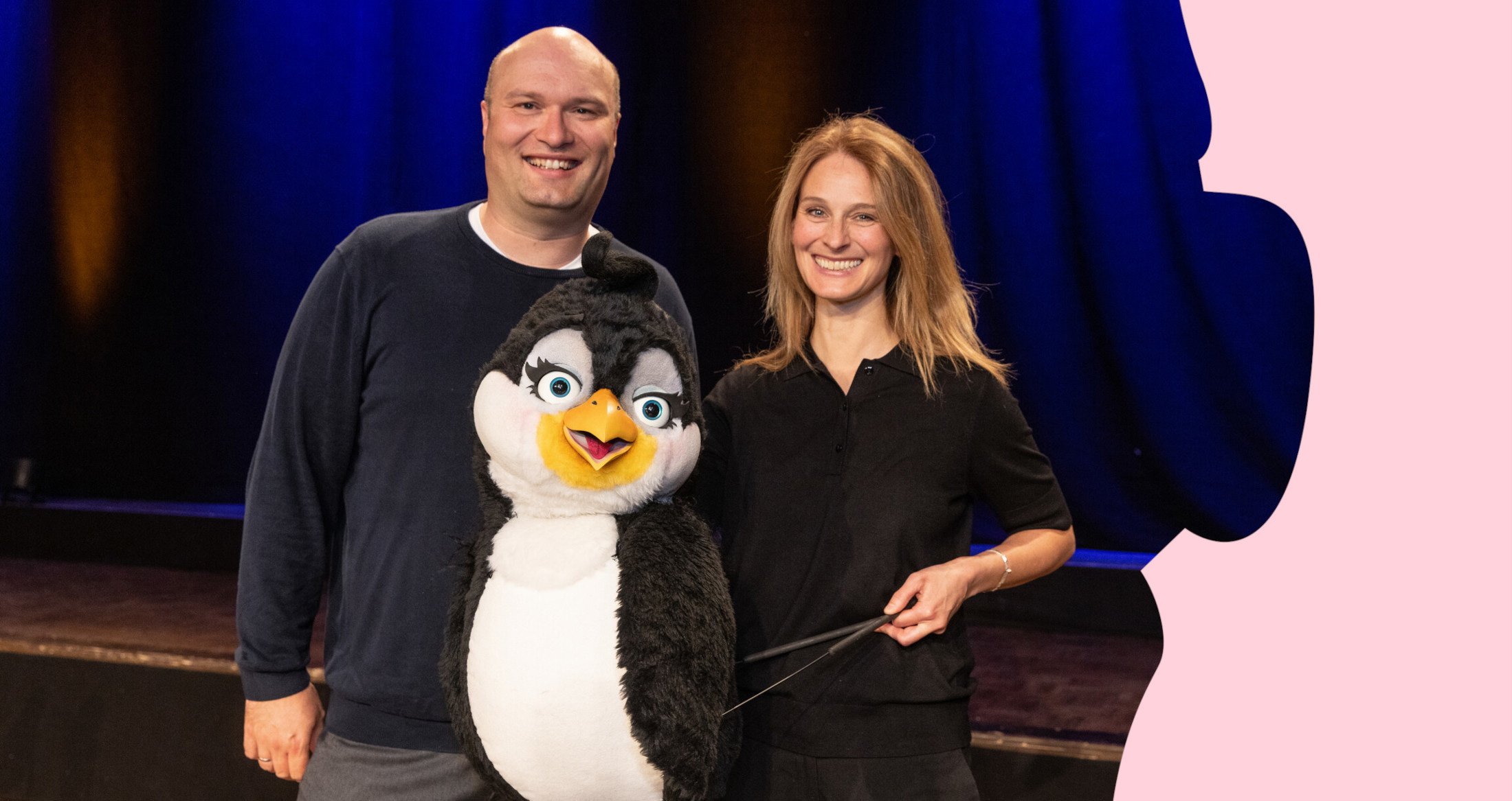 Zwei Personen die in der Mitte eine Pinguin Marionette halten