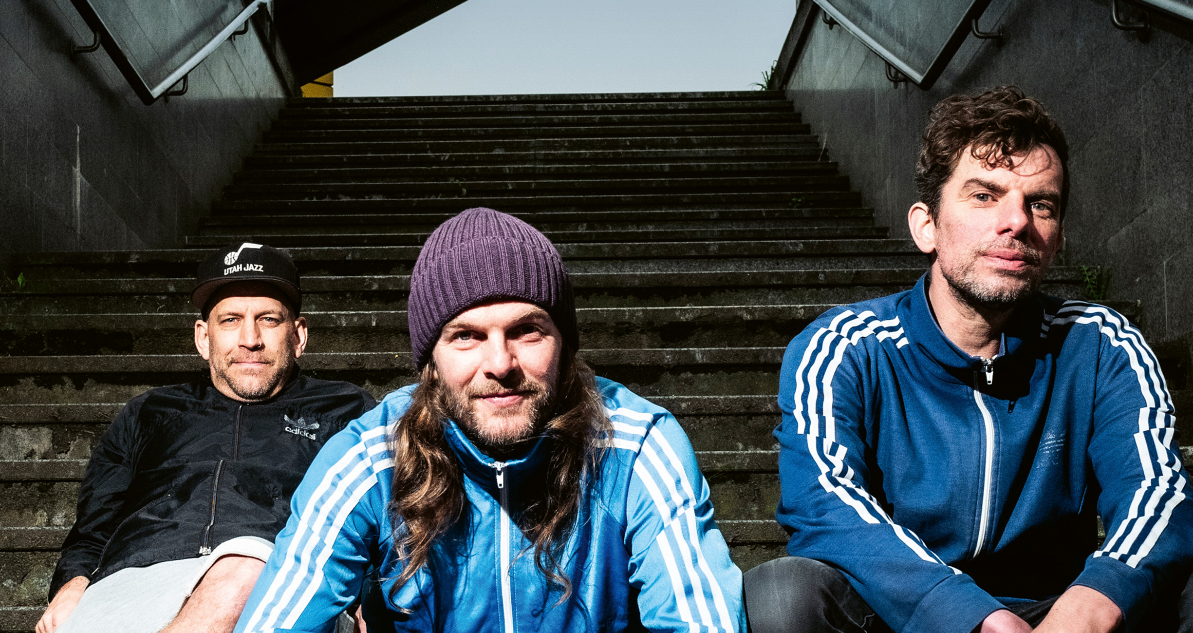 Die drei Mitgleieder der Sportfreunde Stiller sitzen nebeneinander auf Treppenstufen und schauen in die Kamera.