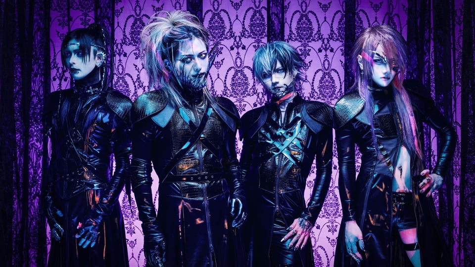 Vier Personen stark geschminkt in schwarzen, futuristischen Outfits mit auffälligen Frisuren und Metall-Accessoires vor violett gemusterter Wand mit Ornamenten in blau‑lila Licht