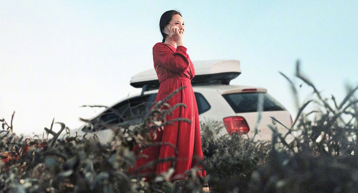 Frau in rotem Kleid vor einem weissen Auto mit dem Handy in der Hand