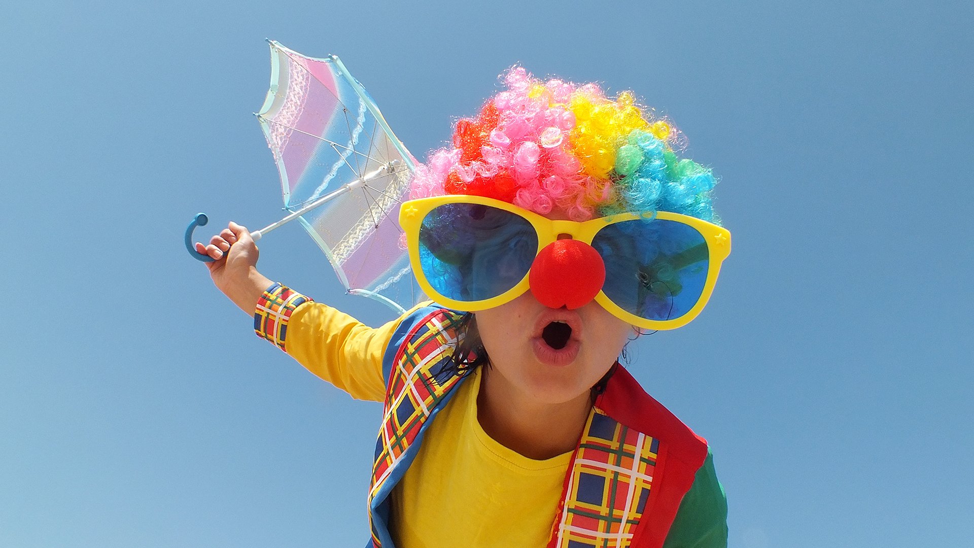 Foto für die Veranstaltung AWO Kinderfasching mit einer als Clown verkleideten Person mit einem Regenschirm vor blauem Hintergrund.