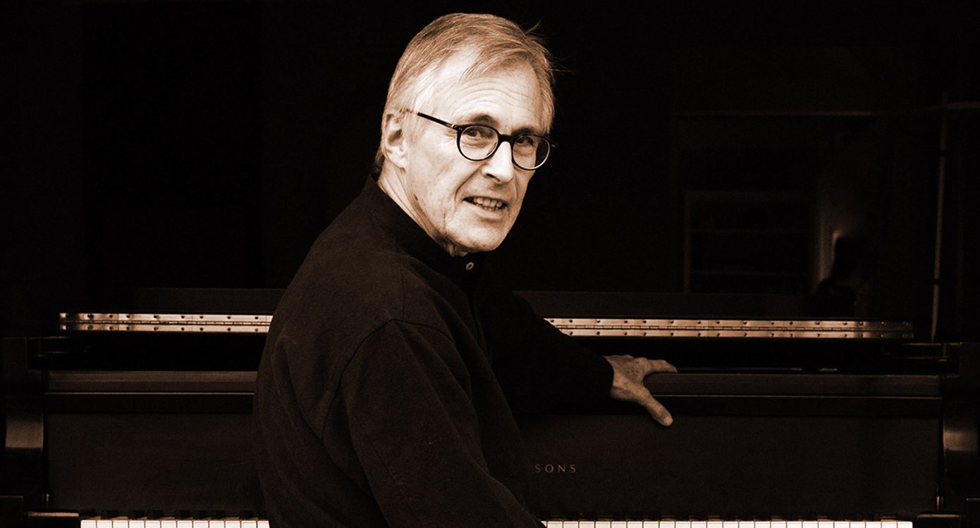 Foto von „Christian Zacharias“, sitzend an einem Klavier auf schwarzem Hintergrund