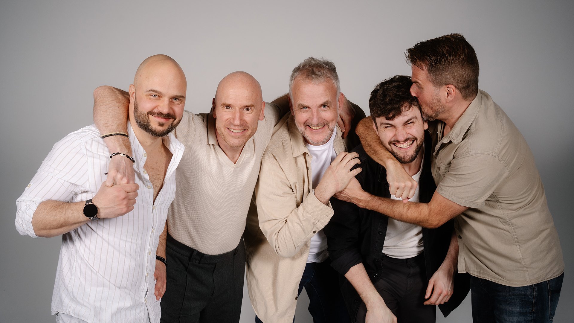 Die Mitglieder der Band Alte Bekannte stehen lachend zusammen vor hellgrauem Hintergrund
