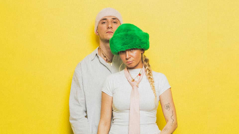 Zwei Künstler in weiß gekleidet vor gelbem Hintergrund