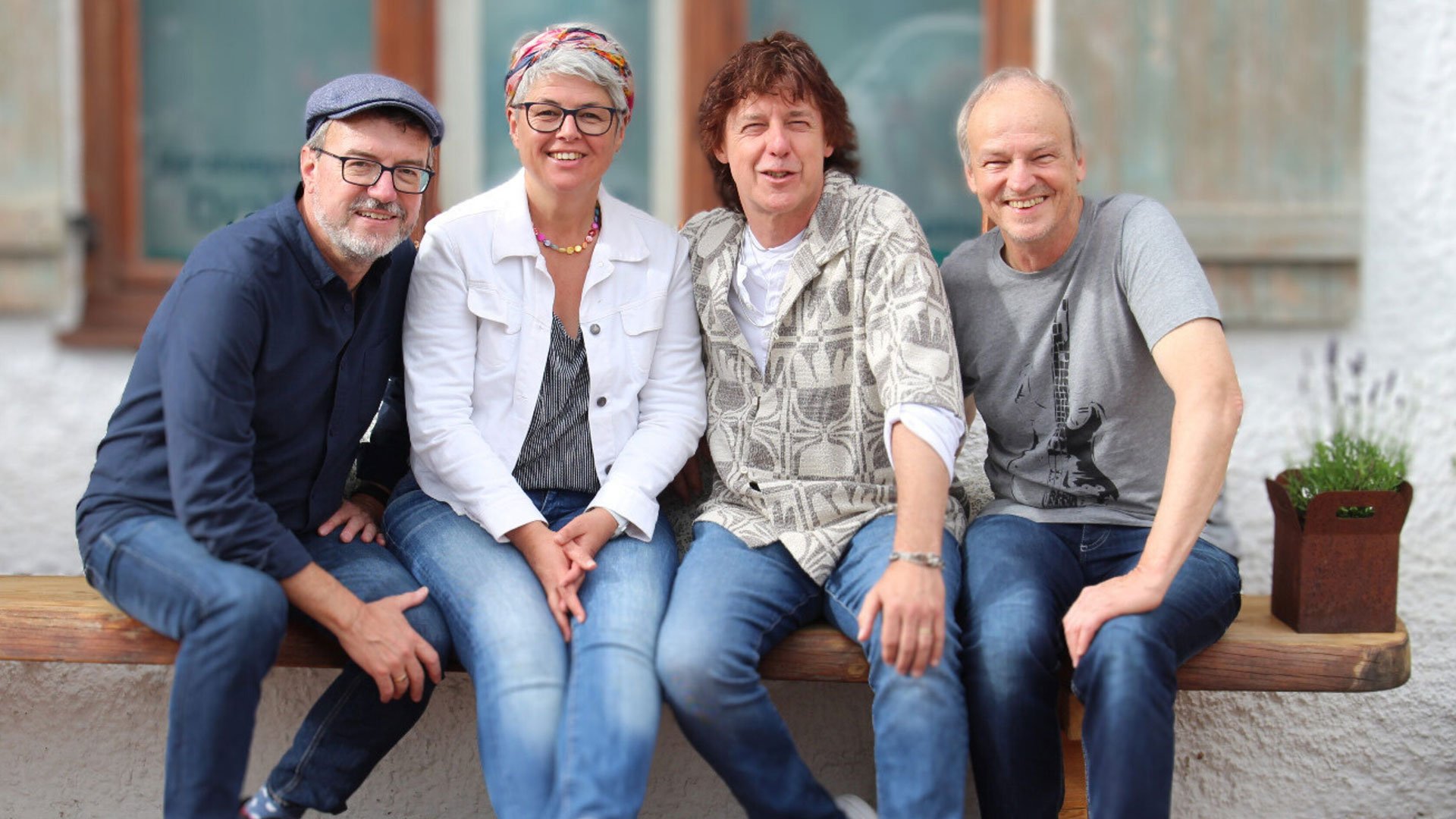 Foto für die Veranstaltung von Schmidtanand mit den vier Künstlern, die auf einer Holzbank sitzen, und einem Fenster im Hintergrund