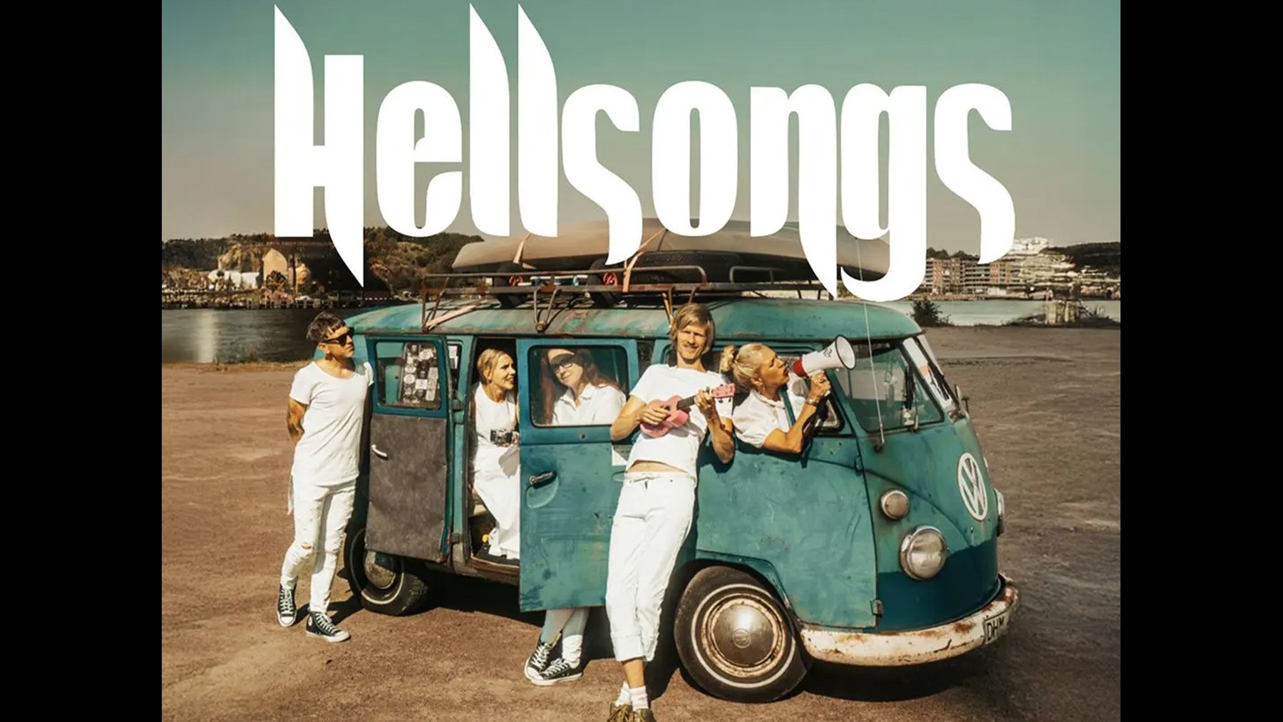 Bandfoto mit mehreren Personen in weißen Outfits an und in einem türkisfarbenen Vintage‑Bus am Wasserufer; im Vordergrund eine Person mit Ukulele, darüber der Schriftzug HELLSONGS