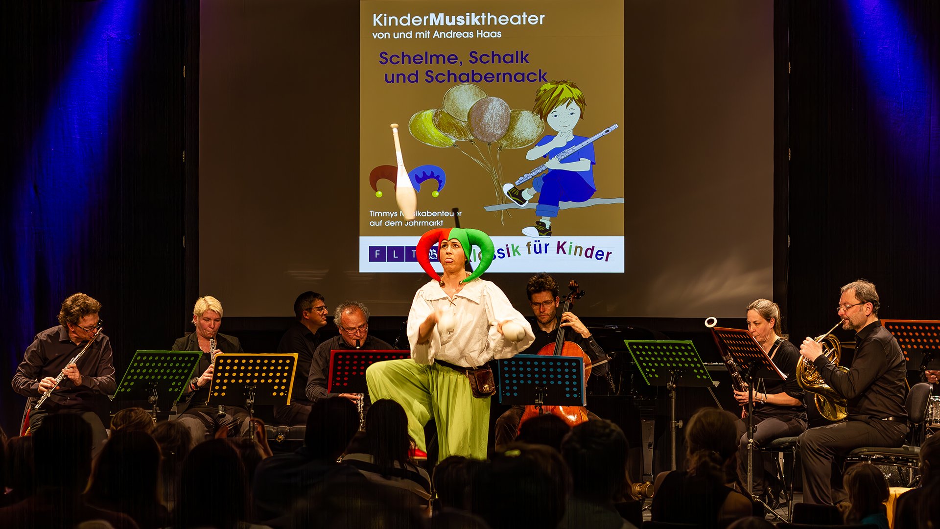 Kinder-Musiktheater auf der Bühne mit Ensemble und Figur im bunten Kostüm
