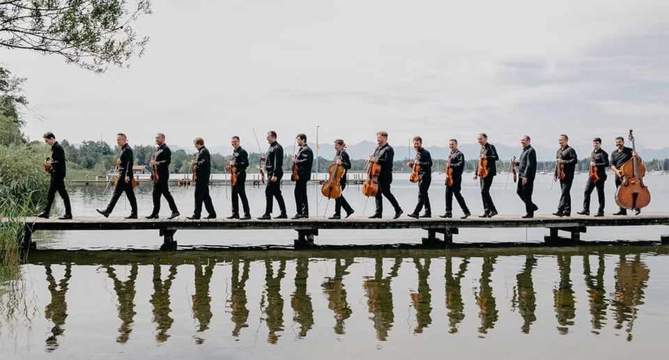 Foto des Orchesters an einem See mit Spiegelung im Wasser