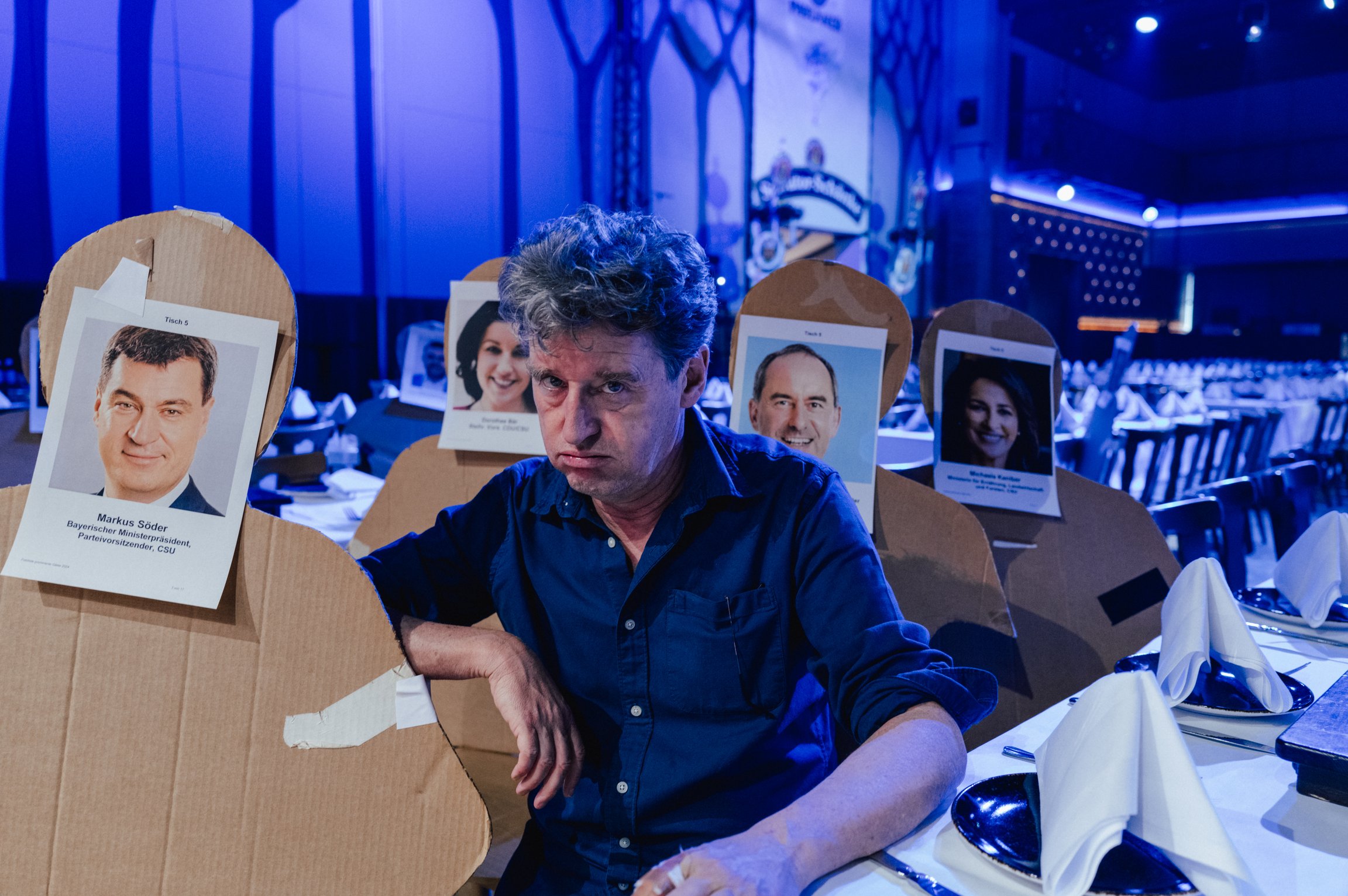 Der Künstler an einem Tisch mit Pappaufstellern von Politikern