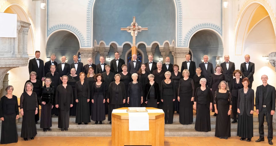 Die Sänger*innen des Lassus Chor in schwarz gekleidet vor einem Kreuz
