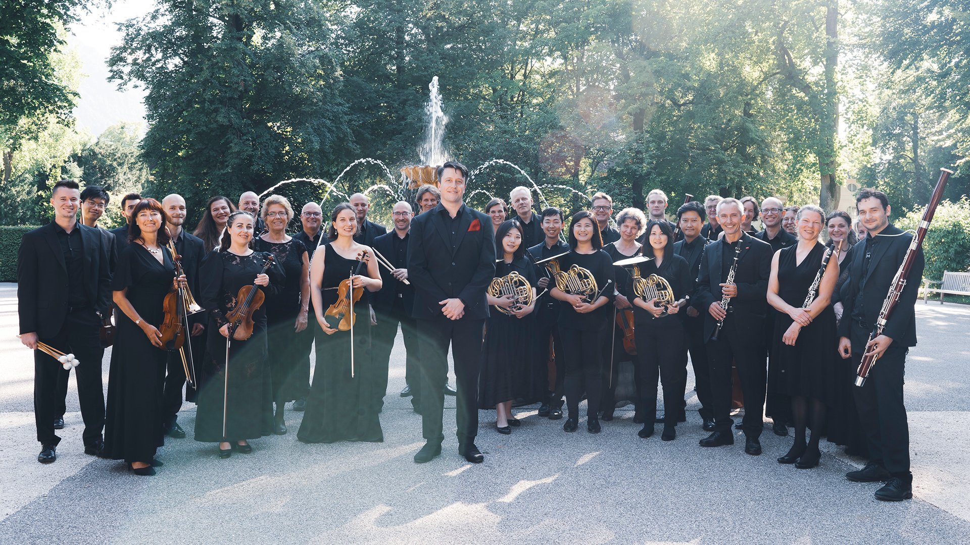 Das Orchester schwarz gekledet mit Instrumenten in einem Park