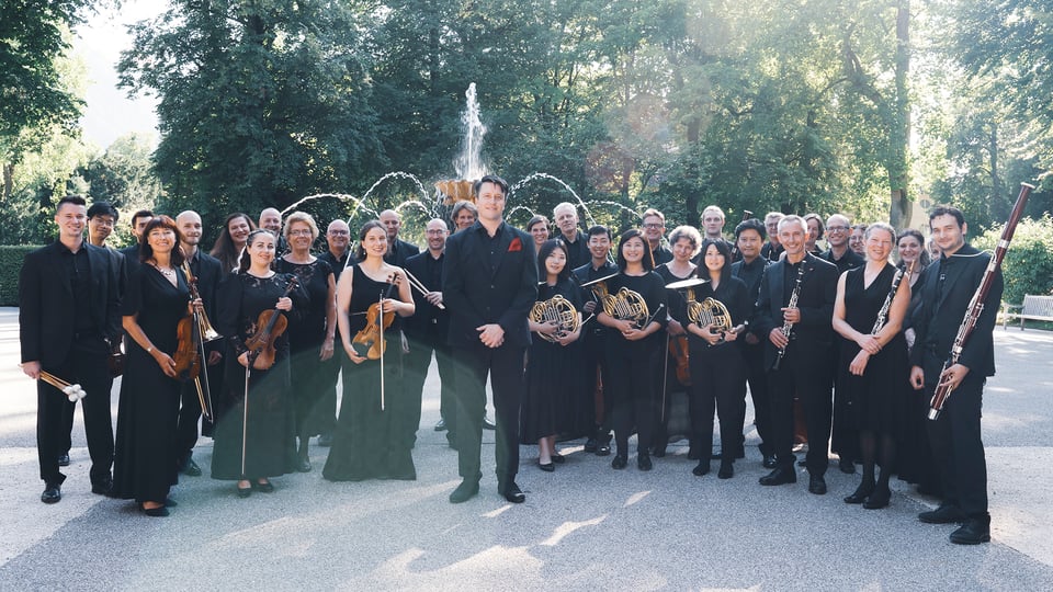 Das Orchester schwarz gekledet mit Instrumenten in einem Park