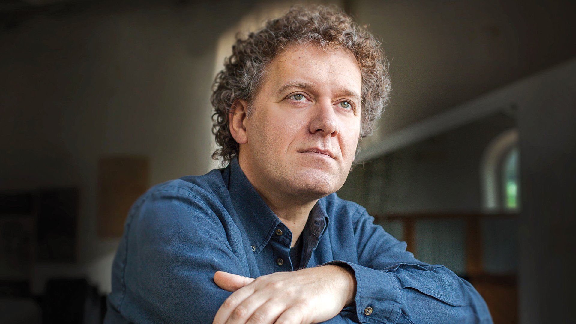 Foto für die Veranstaltung ‚Italienisches Virtuosenkonzert‘ – der Künstler mit blauem Hemd vor dunklem Hintergrund