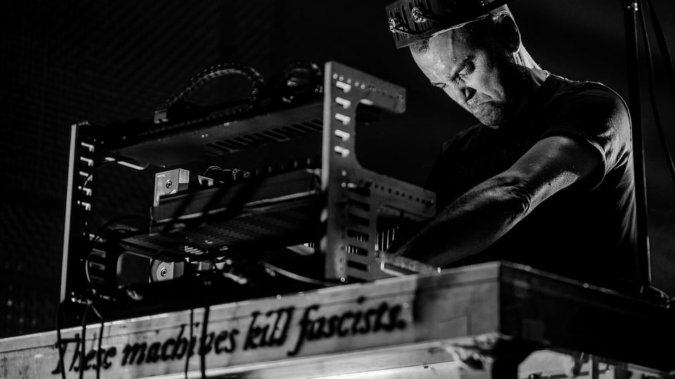 Person bedient eine elektronische Live‑Maschine bei einer industriellen Musikperformance in Schwarz‑Weiß.