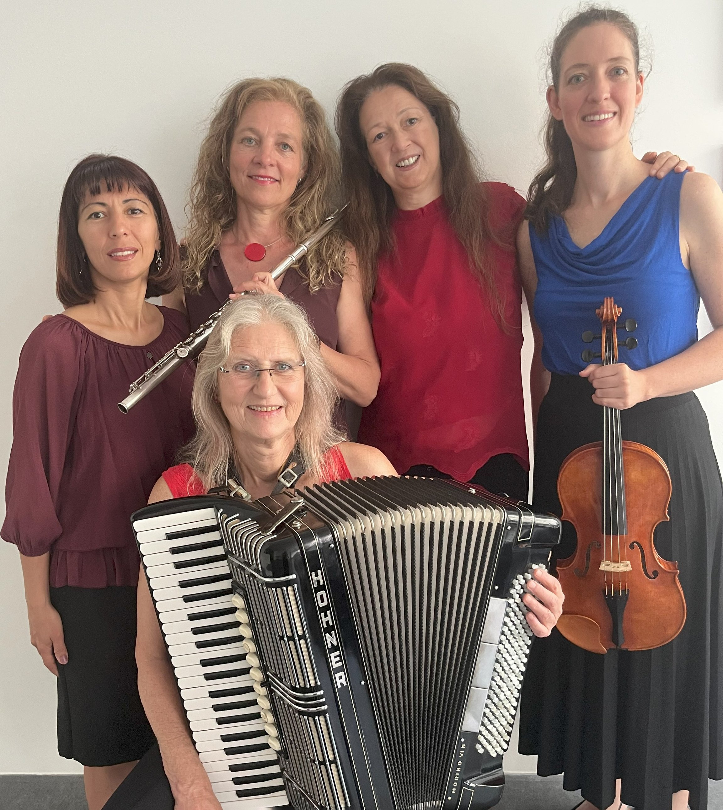 Foto von fünf Frauen mit Instrumenten vor einer weißen Wand