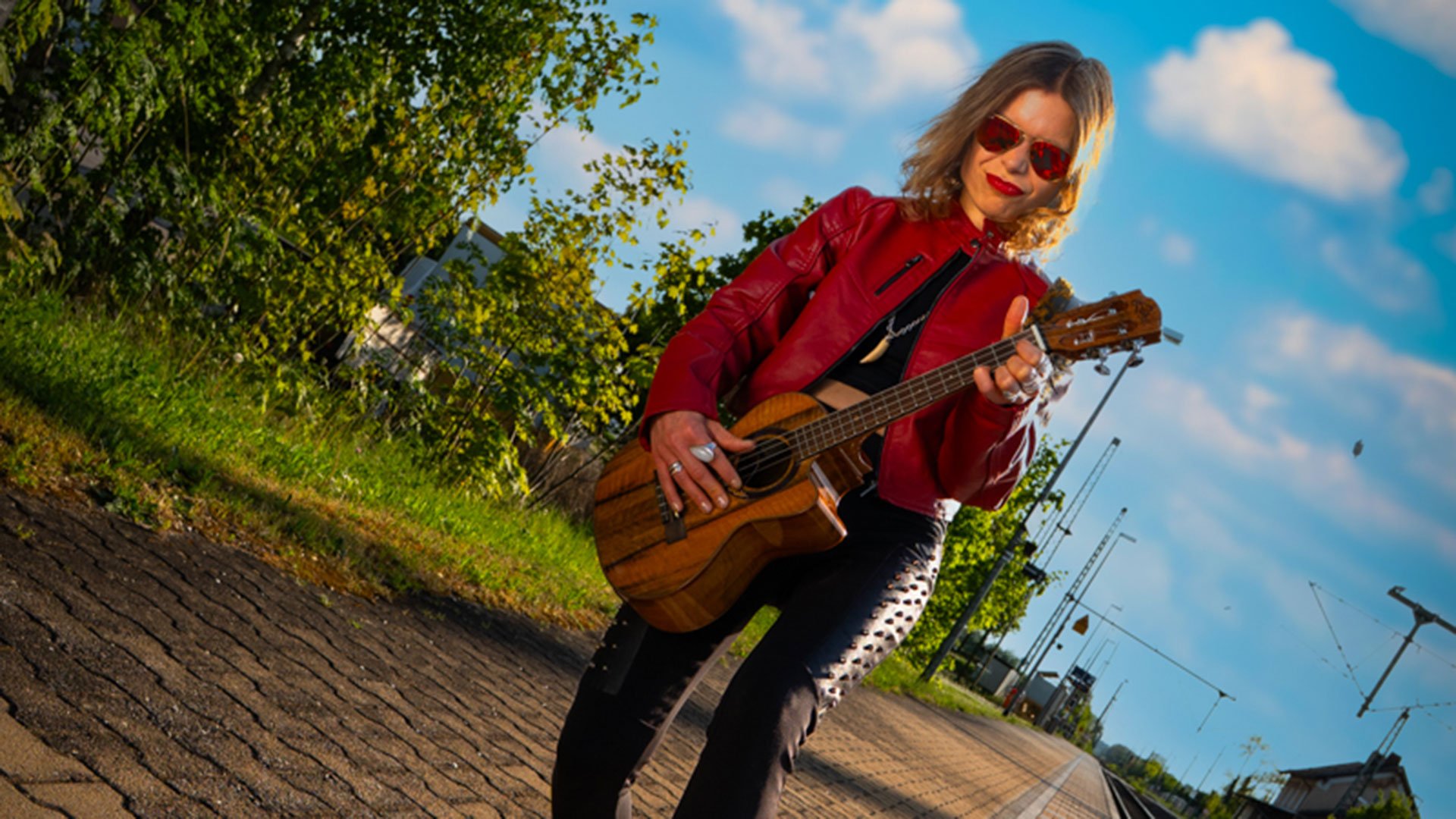 Foto für die Veranstaltung von Andrea Limmer mit der Künstlerin mit einer Gitarre neben den Bahngleisen