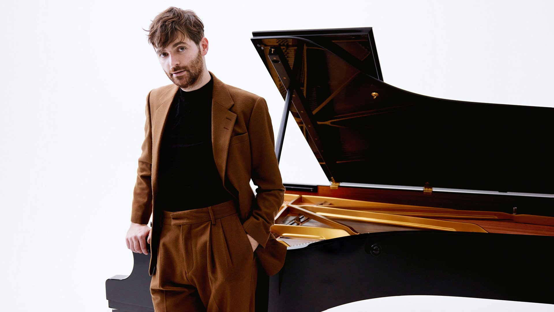 Foto von Florian Christl mit dem Künstler und einem Piano im Hintergrund.