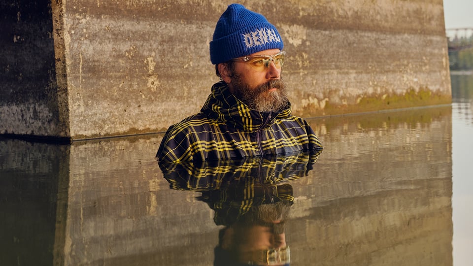 Ein Bild des Künstlers mit blauer Mütze bis zur Brust in Wasser stehend und Spiegelung im Wasser
