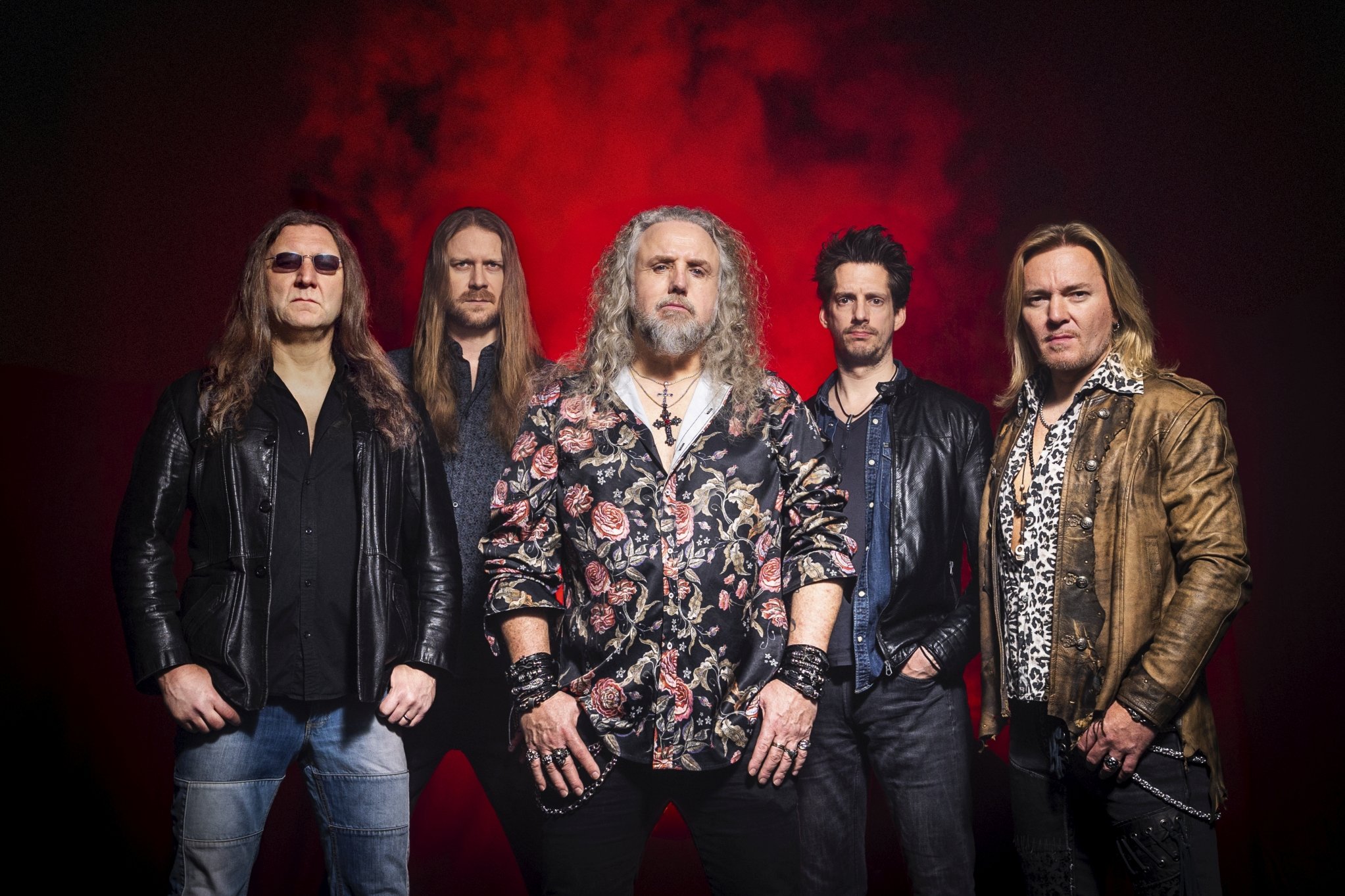 Die Tribute-Band DIO Alive posiert gemeinsam vor dunklem Hintergrund und präsentiert sich im Stil der Hard-Rock-Legende Ronnie James Dio.