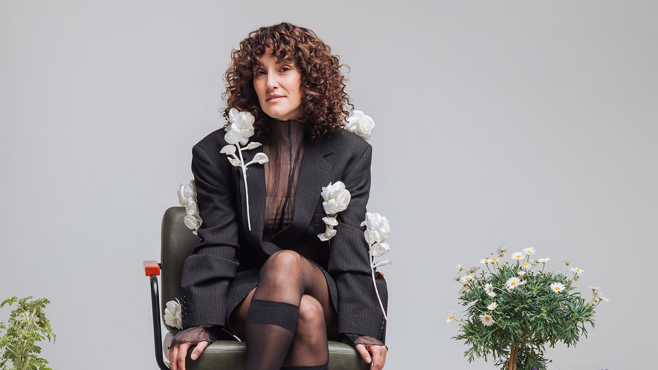 Die Künstlerin auf einem Stuhl sitzend mit weißen Blüten an der Kleidung