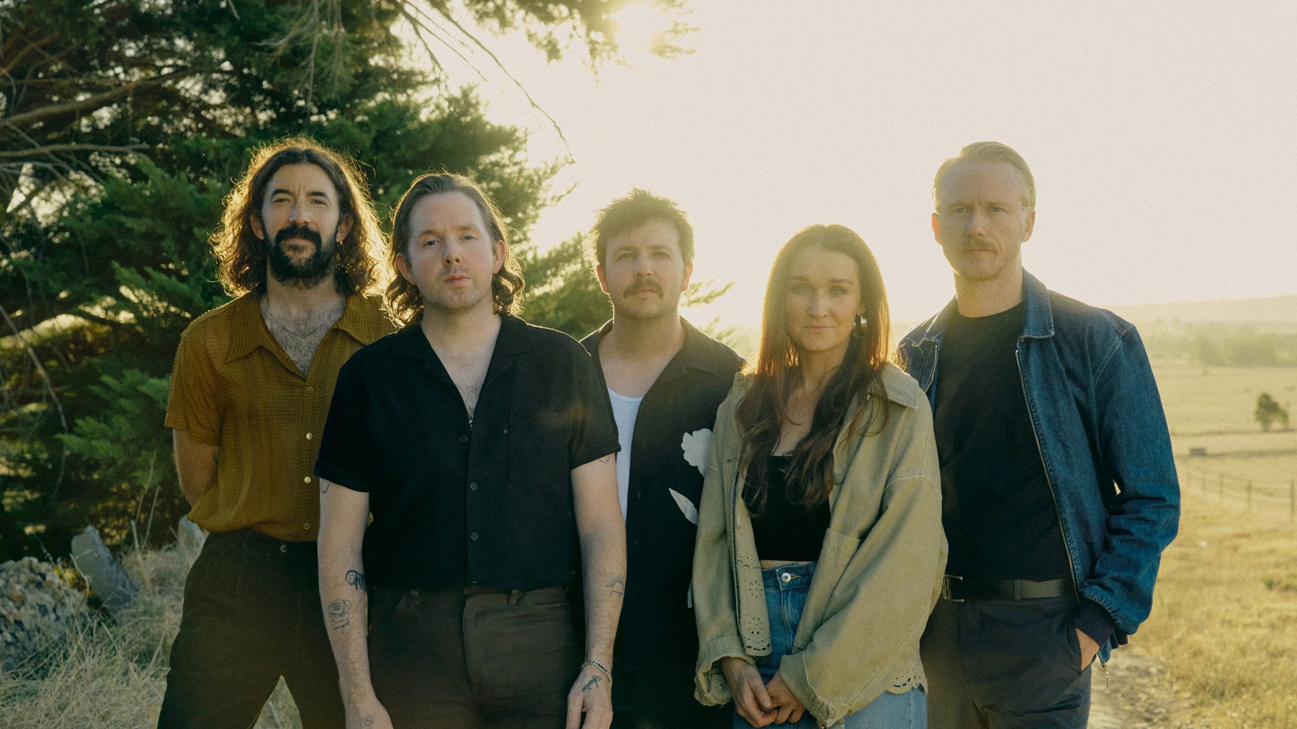 The Paper Kites stehen auf einem Feld vor einem Baum in der Sonne