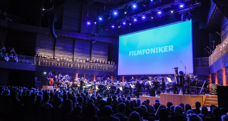Ein Foto eines Orchesters auf einer Bühne mit einer riesigen Leinwand und Publikum