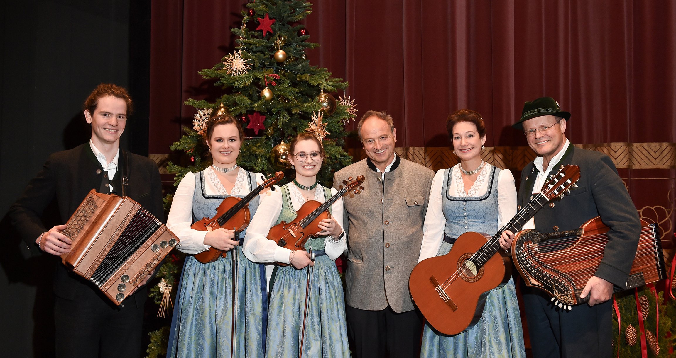 Foto der Gruppe mit Instrumenten in traditionellen bayerischen Trachten vor einem Weihnachtsbaum.