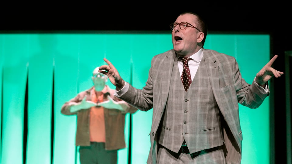 Der Darsteller auf der Bühne mit türkisfarbenem Hintergrund 