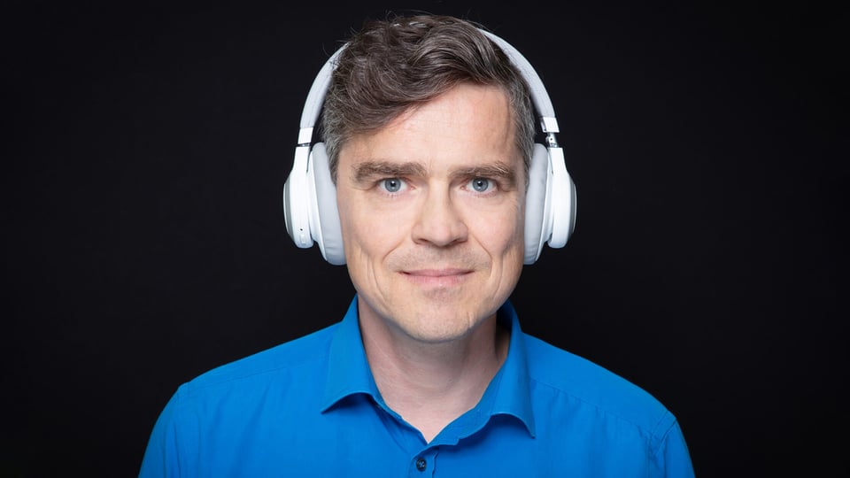 Foto für die Veranstaltung Henning Schmidtke mit dem Künstler, der weiße Kopfhörer trägt, vor schwarzem Hintergrund